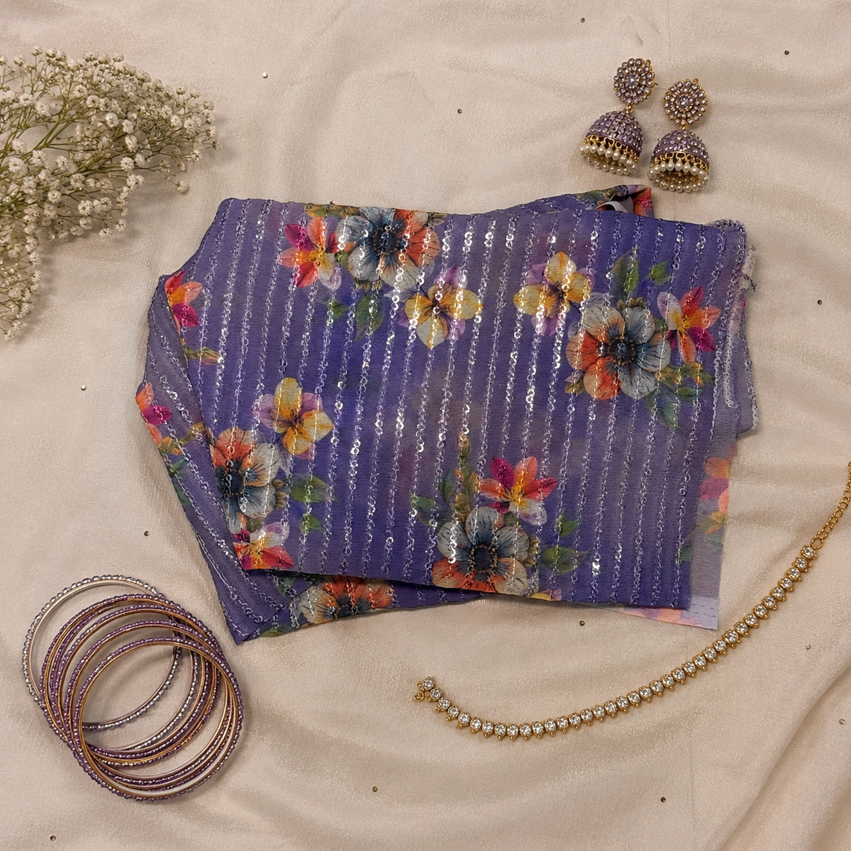 blouse material with vertical metallic silver stripes and a colorful floral print, styled on a beige fabric background with traditional Indian jewelry and floral props.