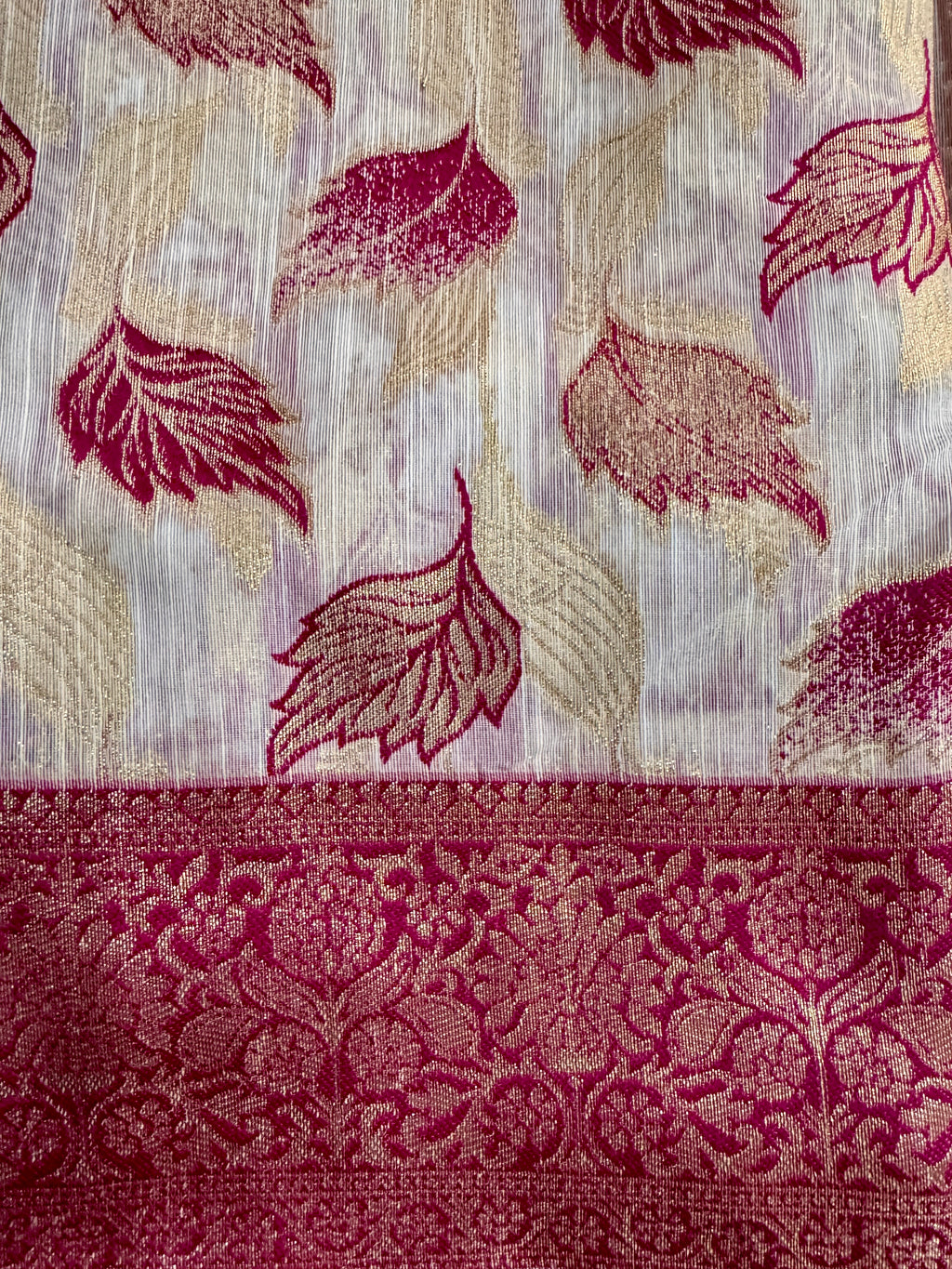 A close-up of a woven textile with a white base, burgundy leaf motifs, and a wide matching burgundy floral border.